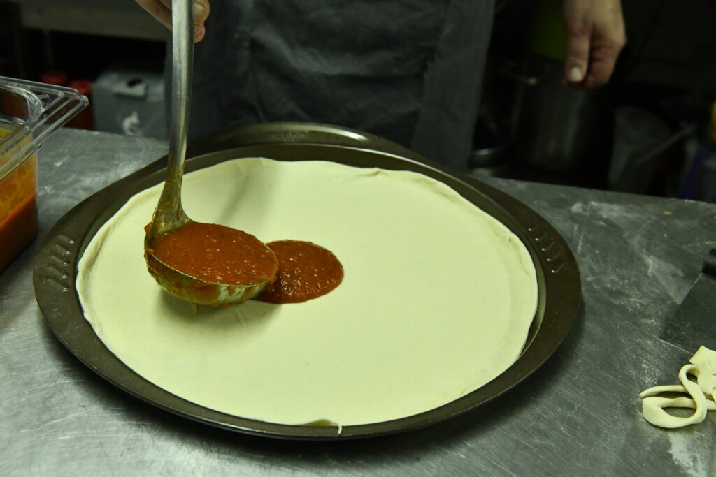 Ajout de la sauce tomate sur la pizza à la coppa