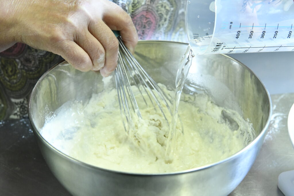 Ajout de farine, d'eau dans un saladier pour pate à beignets de poireaux recette corse