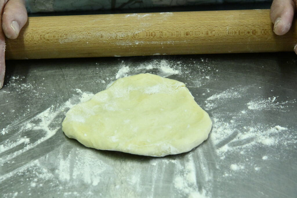 Applatir au rouleau une boule de pate brisée sur un plan de travail fariné pour de délicieux bastelle